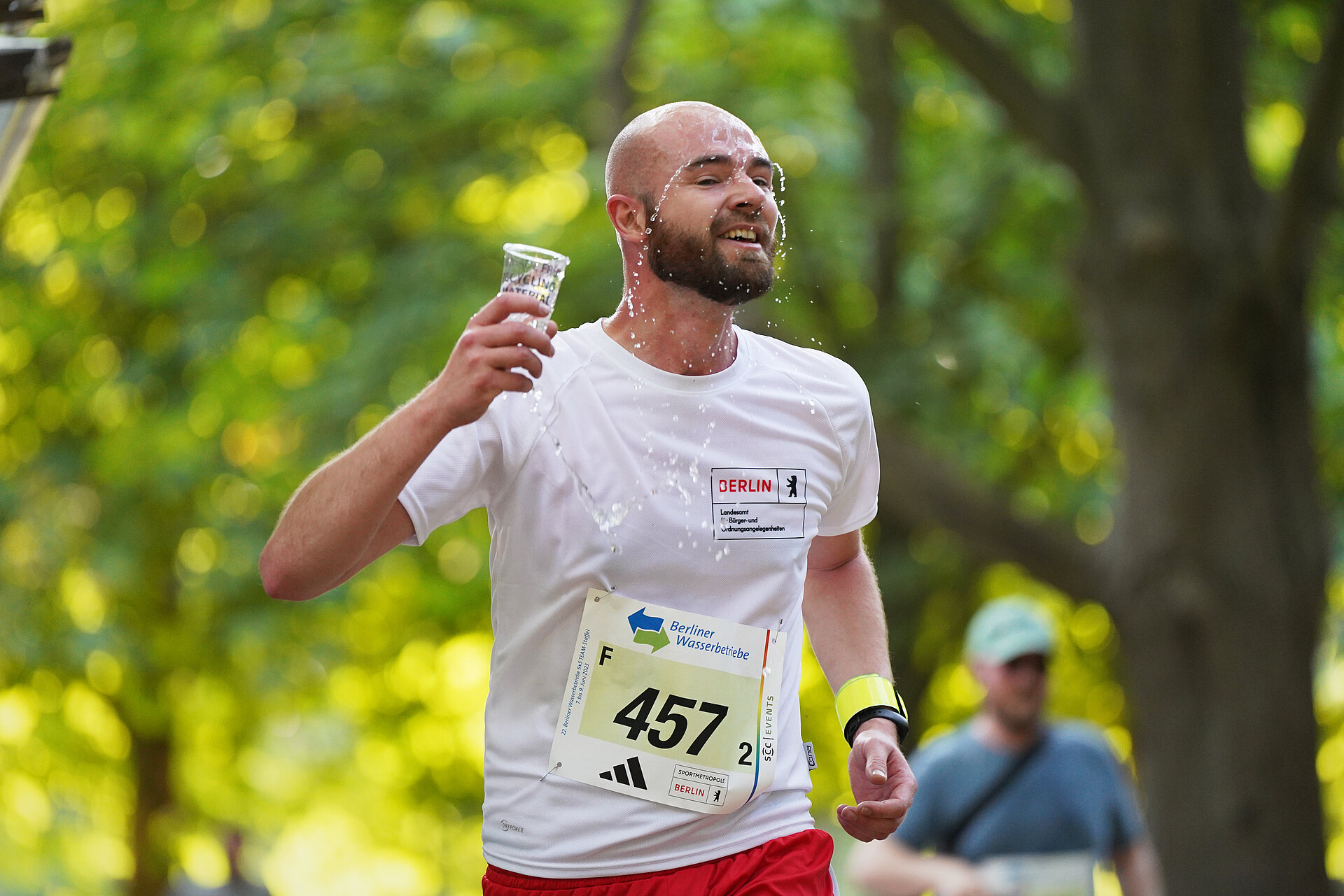 5x5 km TEAM-Staffel: Männlicher Läufer schüttet sich aus einem Becher Wasser ins Gesicht @ SCC EVENTS / Kai Wiechmann