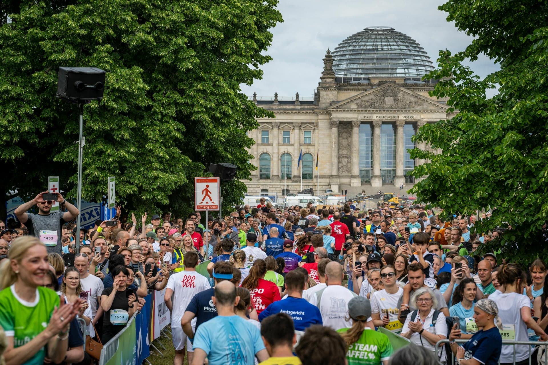 Zahlreiche Läufer:innen auf einem Streckenabschnitt, der genau Richtung Reichtstagsgebäude verläuft. Neben der Strecke stehen dutzende Personen, viele selbst mit Startnummern.