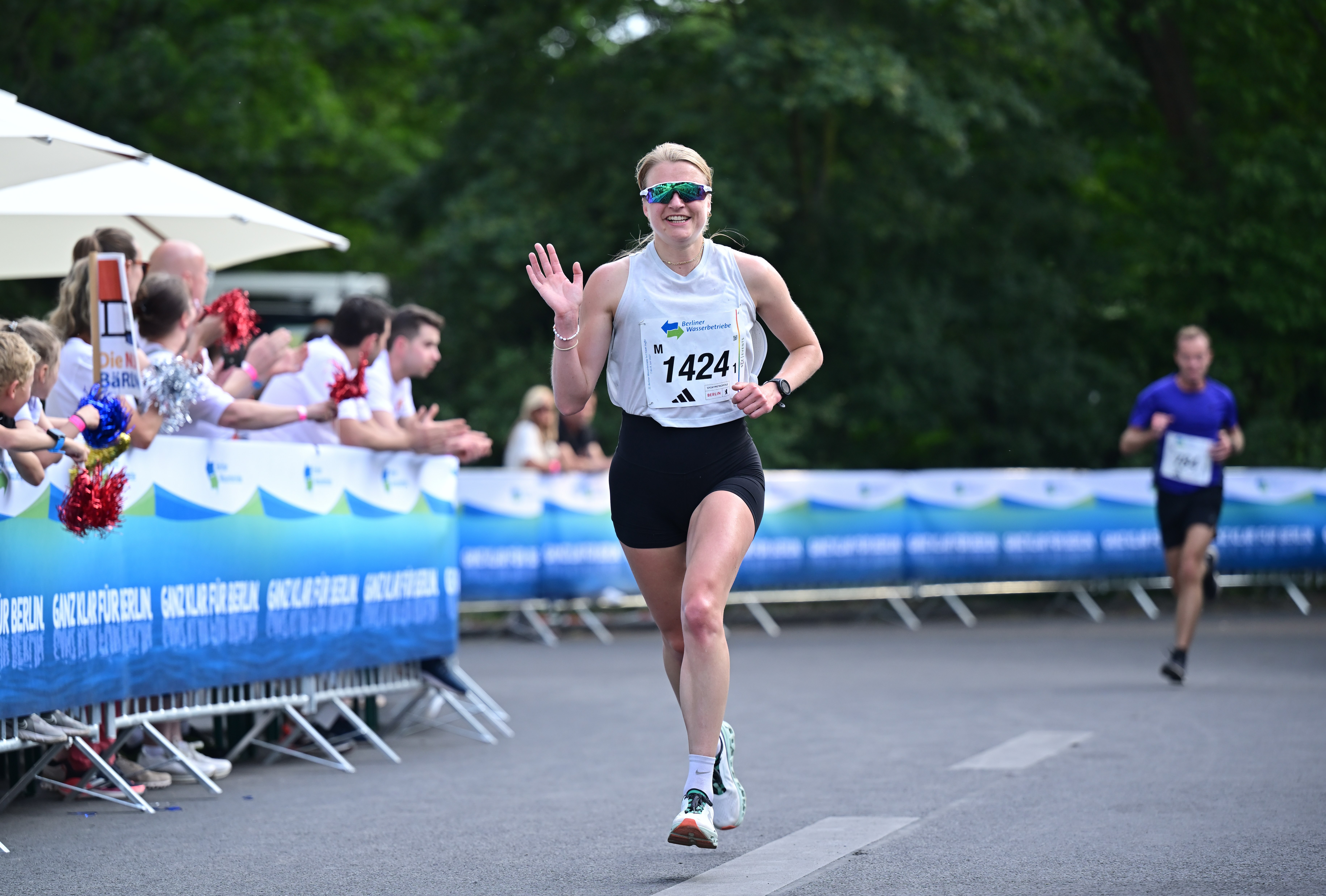 5x5 km TEAM-Staffel: Weiblich Läuferin passiert Zuschauer und winkt in die Kamera @ SCC EVENTS / Petko Beier